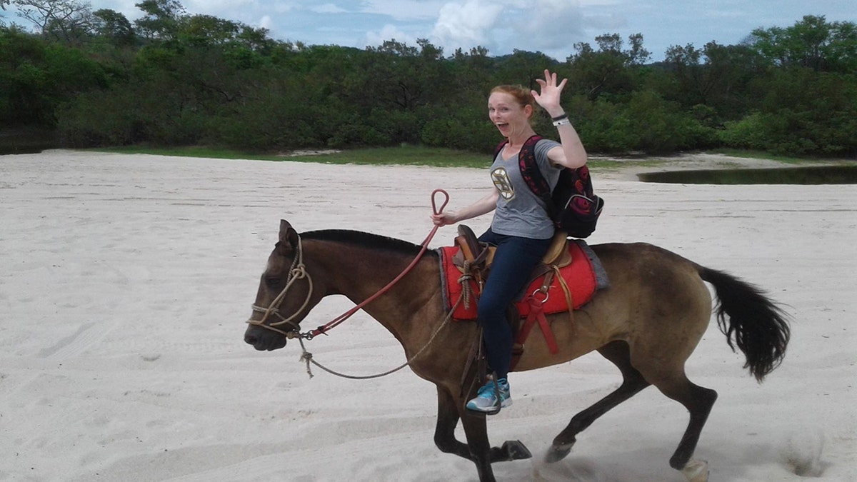 Terillyn Griffiths riding a horse and smiling. The woman is sitting on a horse on the outside as the Galops horse.
